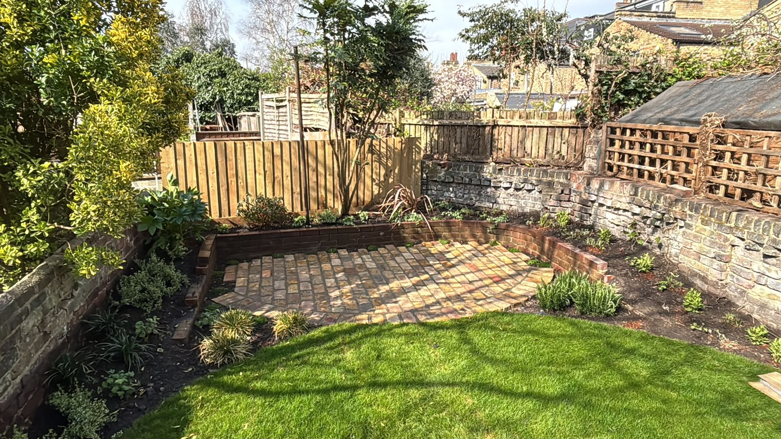A stretcher bond brick terrace curving around a lawn, with new planting set against old brick boundary walls.
